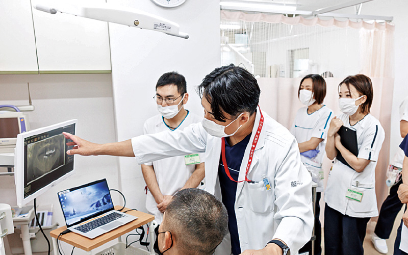 [写真] 口腔のパノラマX線写真を見ながら、患者さんに説明を行う小野先生